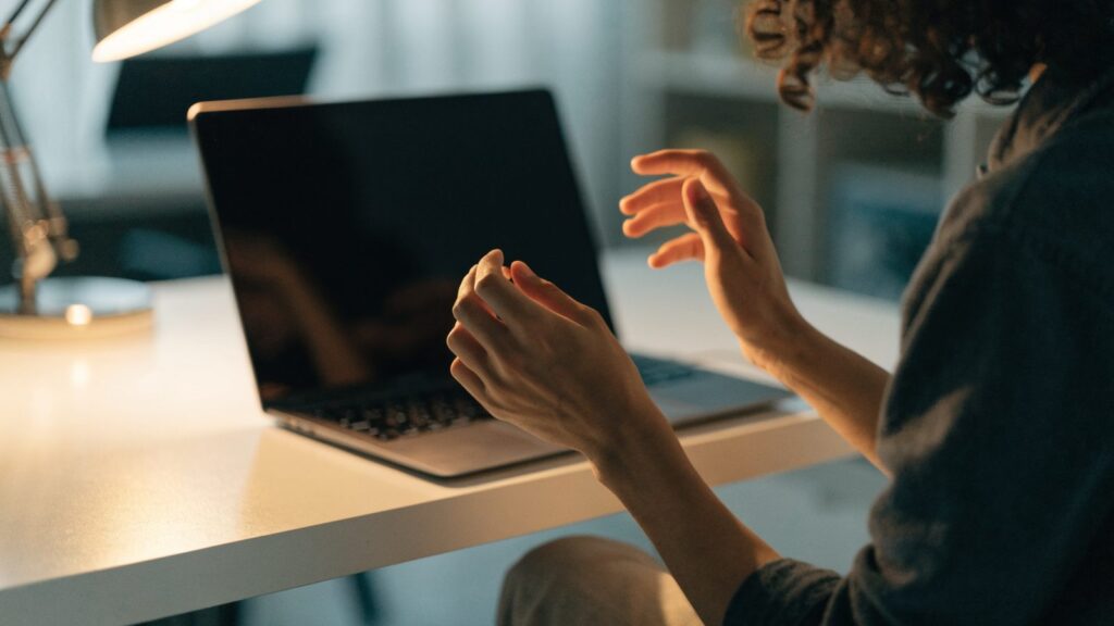 A person seen from behind with hands raised at a graphite black laptop with a dark blank screen on a white des