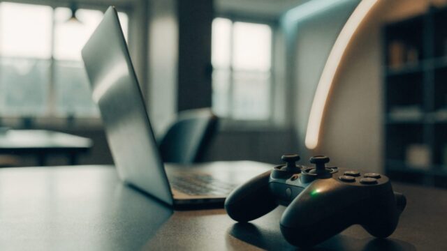 A game controller resting on a desk beside a silver laptop in a room with soft LED glow