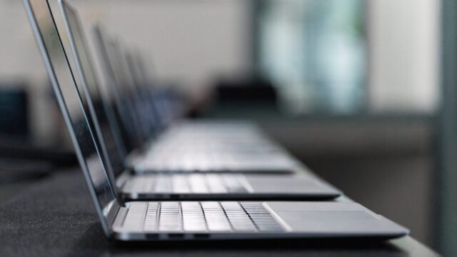 Several modern laptops lined up in a row on a dark desk mat