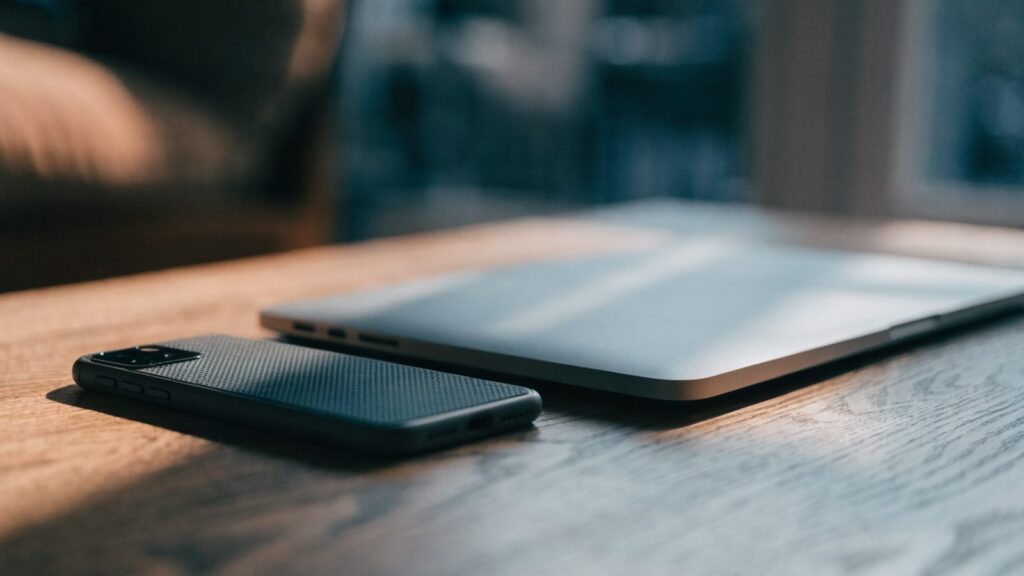 A smartphone lying beside a silver laptop on a wooden desk