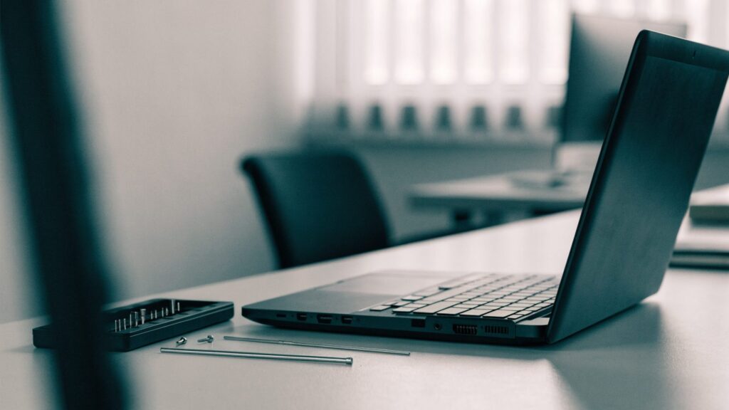A precision screwdriver kit laid out beside a partially opened graphite black laptop on an office desk