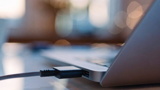 Close-up of a USB-C charger cable plugged into the side port of a silver laptop on a white desk
