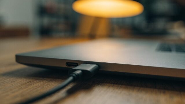 Close-up of a USB-C charger cable plugged into the side port of a matte grey laptop on a wooden desk