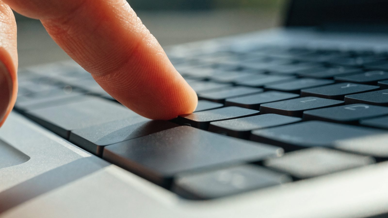 Close-up of a single key being pressed on a silver laptop keyboard