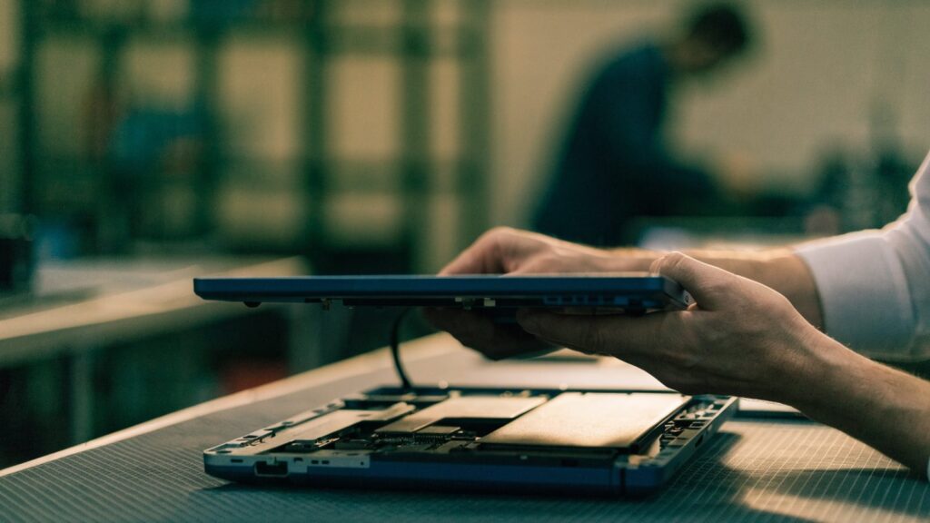 A technician lifting the bottom cover off a dark blue laptop on an anti-static mat