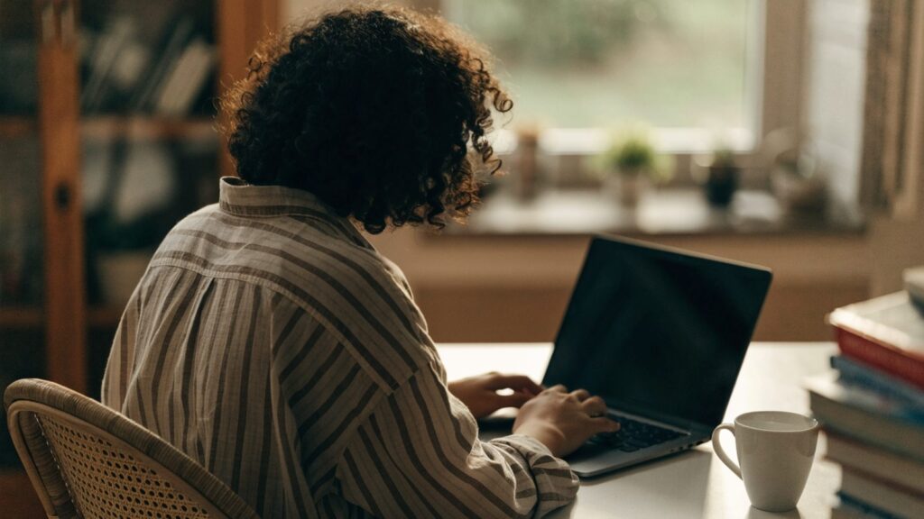 A person seen from behind working on a graphite black laptop in a bright home office