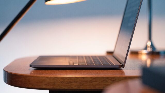 A sleek modern matte grey laptop centered on a wooden desk against a clean soft gradient background