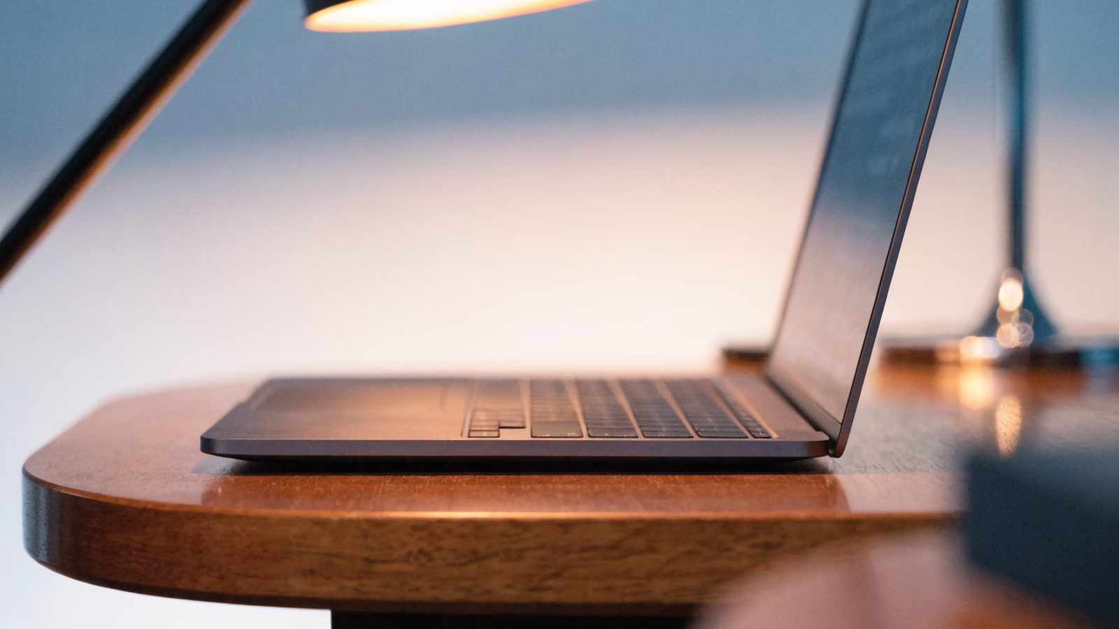 A sleek modern matte grey laptop centered on a wooden desk against a clean soft gradient background