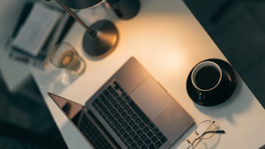 Top-down view of a matte grey laptop on a white desk with a coffee cup and glasses