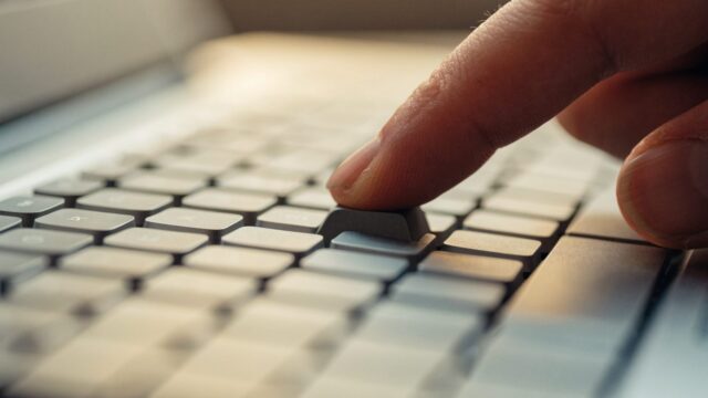 Close-up of a single key being pressed on a silver laptop keyboard