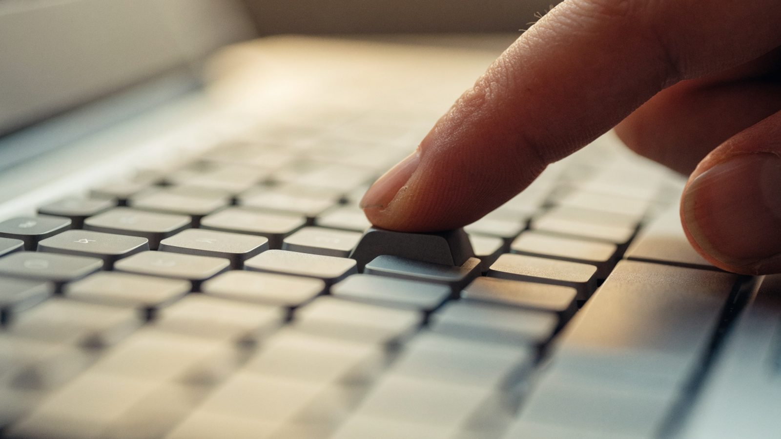 Close-up of a single key being pressed on a silver laptop keyboard