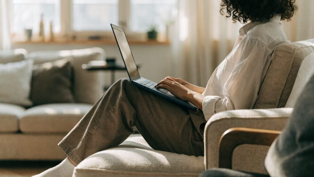 A person seen from behind using a dark blue laptop on a sofa