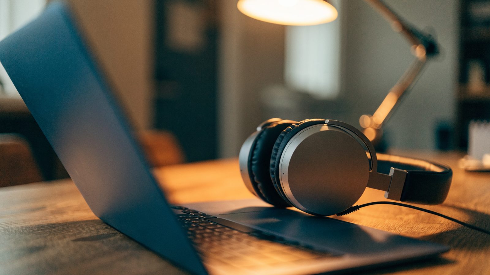 Over-ear headphones resting beside a dark blue laptop on a wooden desk