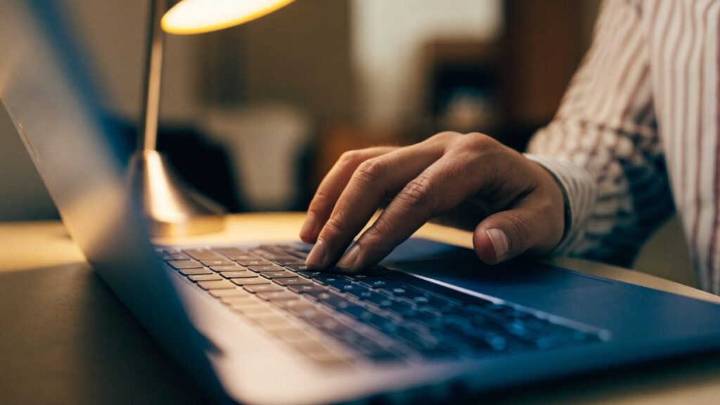 A hand resting on a dark blue laptop trackpad