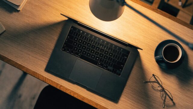 Top-down view of a graphite black laptop on an office desk with a coffee cup and glasses
