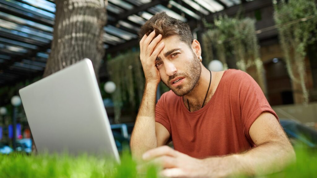 Tired male programmer, IT guy looking exhausted, sitting with laptop outdoor cafe