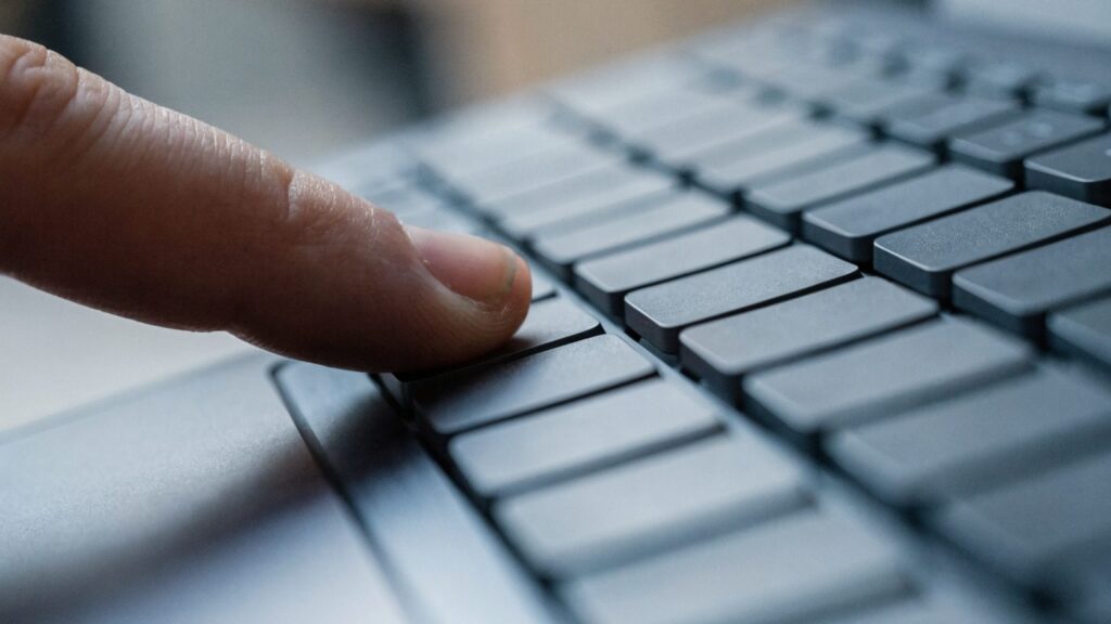 Close-up of a single key being pressed on a matte grey laptop keyboard
