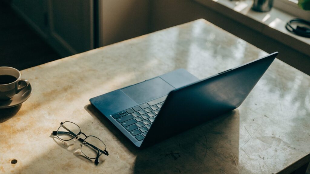 Top-down view of a dark blue laptop on a workbench with a coffee cup and glasses