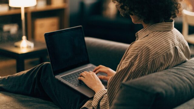 A person seen from behind using a matte grey laptop on a sofa