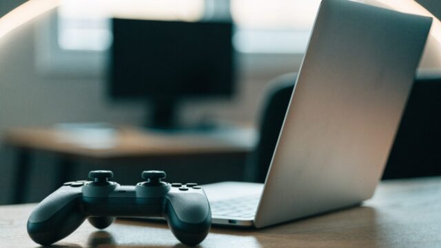 A game controller resting on a desk beside a silver laptop in a room with soft LED glow