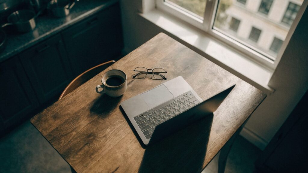 Top-down view of a matte grey laptop on a kitchen table with a coffee cup and glasses