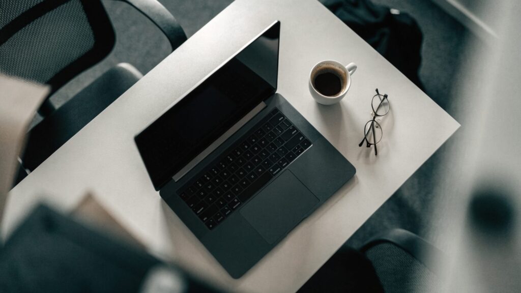 Top-down view of a graphite black laptop on an office desk with a coffee cup and glasses