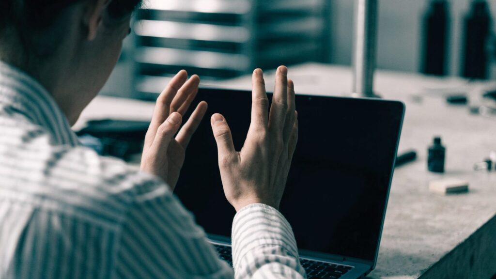 A person seen from behind with hands raised at a dark blue laptop with a dark blank screen on a workbench
