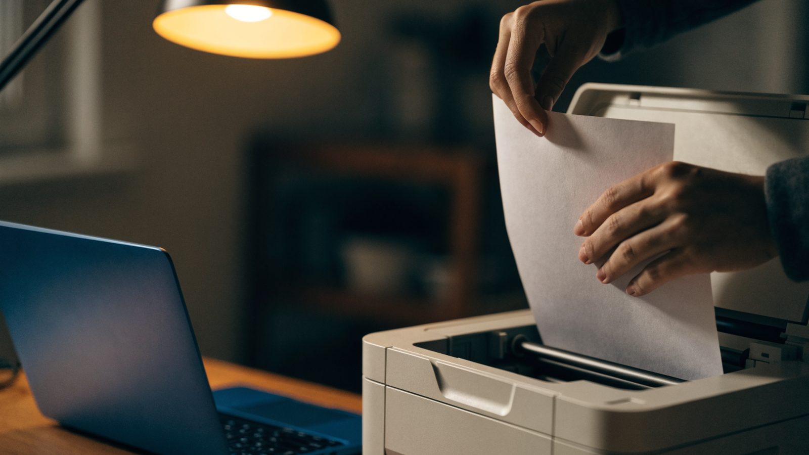 Hands loading blank paper into a small home printer