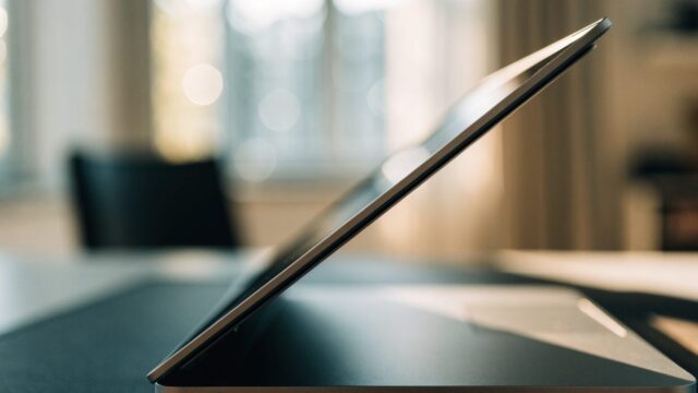 Close-up of the hinge and screen edge of a matte grey laptop on a dark desk mat