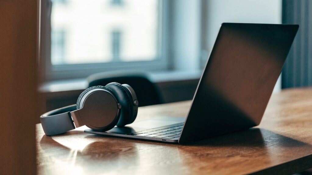 Over-ear headphones resting beside a graphite black laptop on a wooden desk