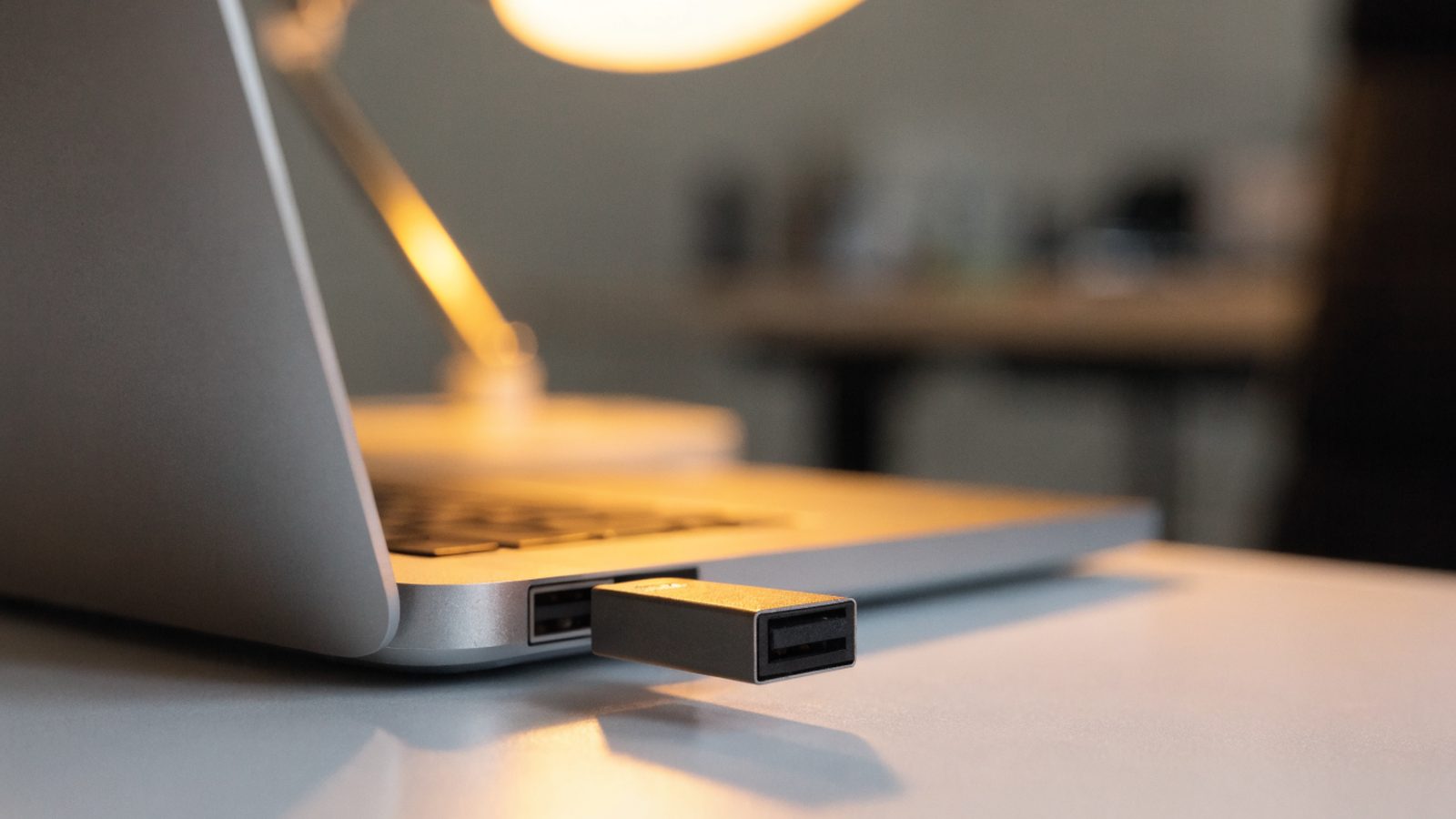 A USB flash drive plugged into the side port of a silver laptop on a white desk