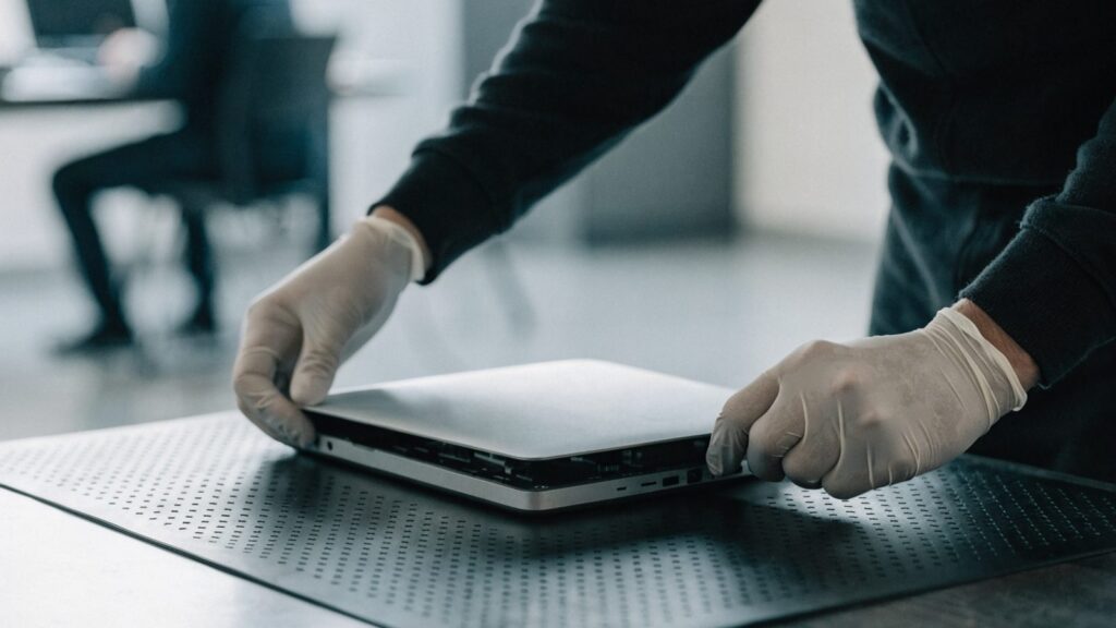 A technician lifting the bottom cover off a silver laptop on an anti-static mat