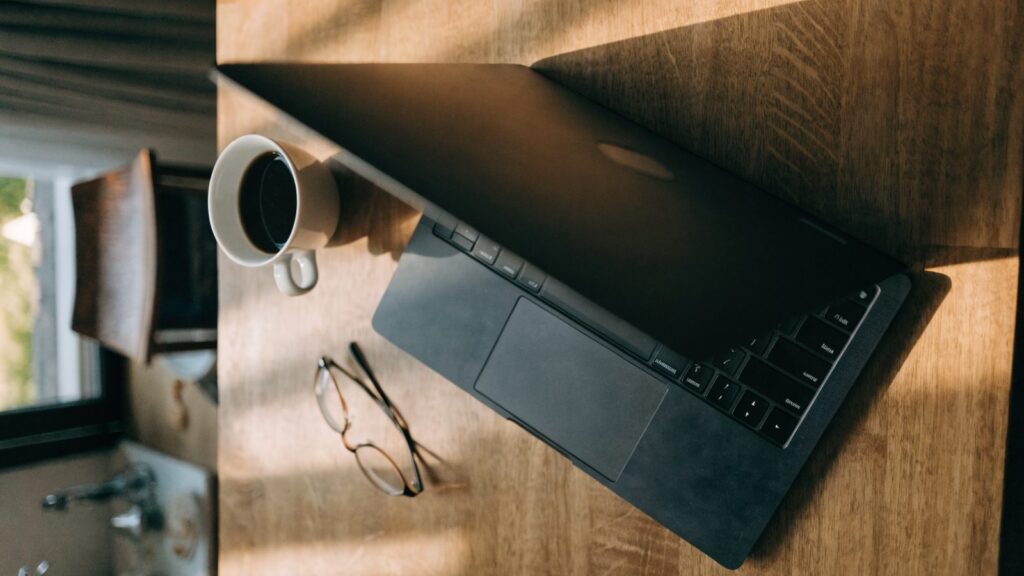 Top-down view of a graphite black laptop on a kitchen table with a coffee cup and glasses