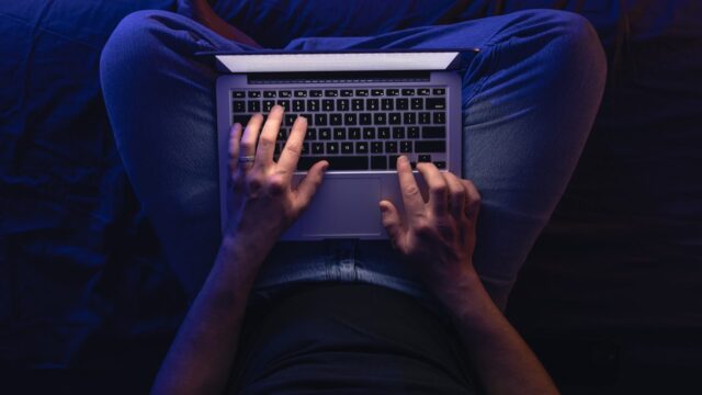 Close up of hacker hand stealing data man networking on laptop late at night