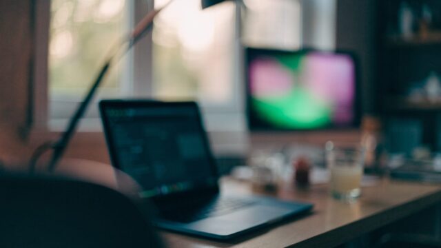 A developer's desk at night with a dark blue laptop and a second monitor showing soft blurred colorful glow