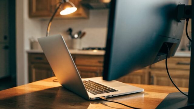 A silver laptop connected to a large external monitor with a blank dark screen via a cable on a kitchen table