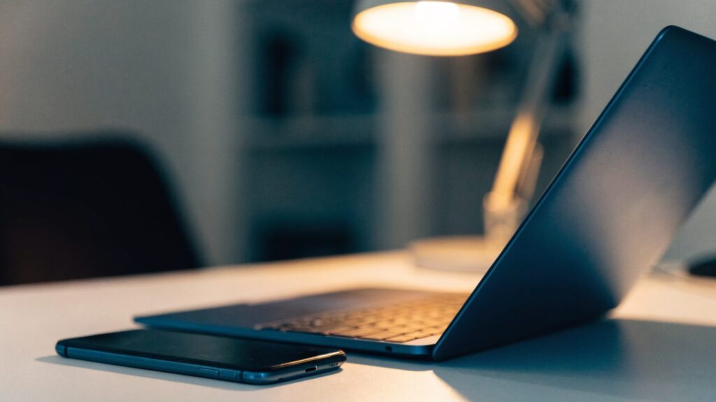 A smartphone lying beside a dark blue laptop on a white desk
