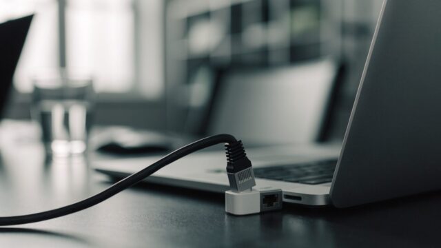 An ethernet cable being plugged into a USB-C adapter connected to a silver laptop on an office desk