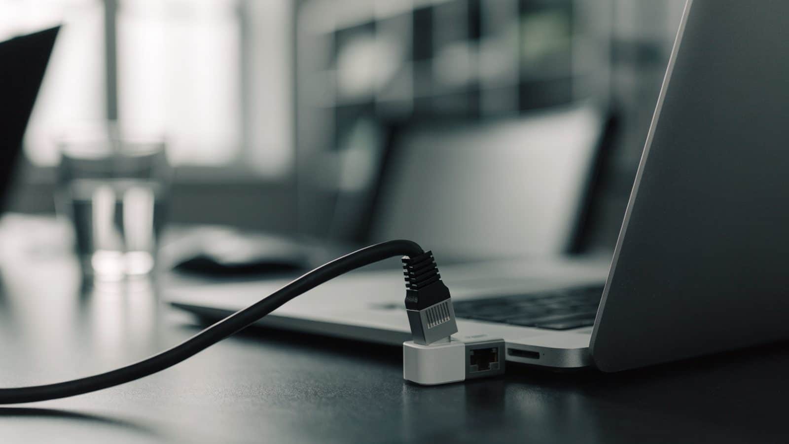 An ethernet cable being plugged into a USB-C adapter connected to a silver laptop on an office desk