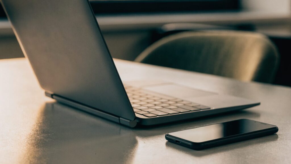 A smartphone lying beside a graphite black laptop on an office desk