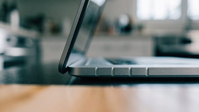 Close-up of the hinge and screen edge of a silver laptop on a kitchen table