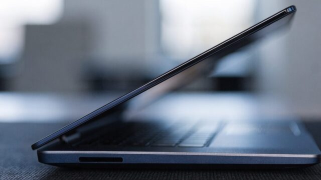 Close-up of the hinge and screen edge of a dark blue laptop on a dark desk mat