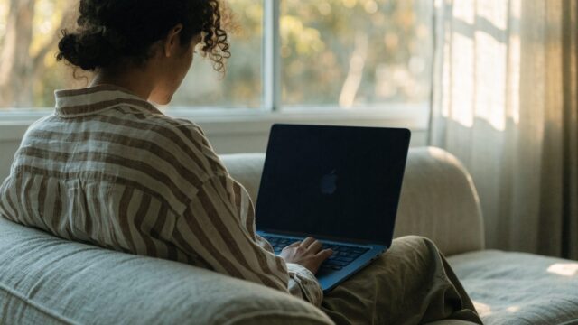 A person seen from behind using a dark blue laptop on a sofa