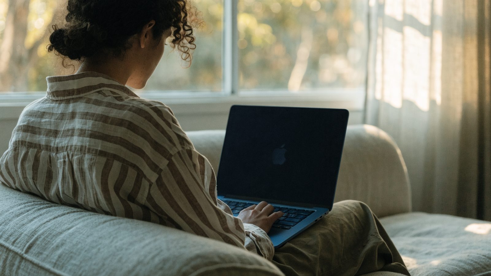 A person seen from behind using a dark blue laptop on a sofa