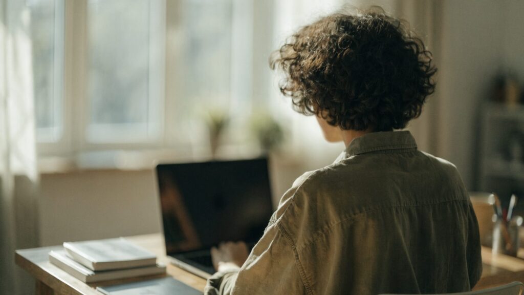 A person seen from behind working on a graphite black laptop in a bright home office