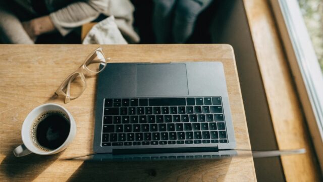 Top-down view of a matte grey laptop on a kitchen table with a coffee cup and glasses
