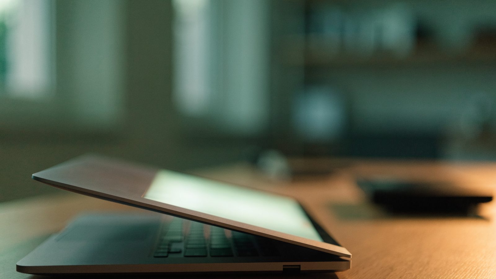 A half-closed matte grey laptop on a wooden desk