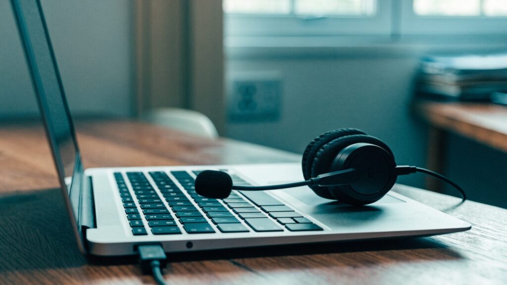 A USB headset with microphone plugged into a silver laptop on a wooden desk