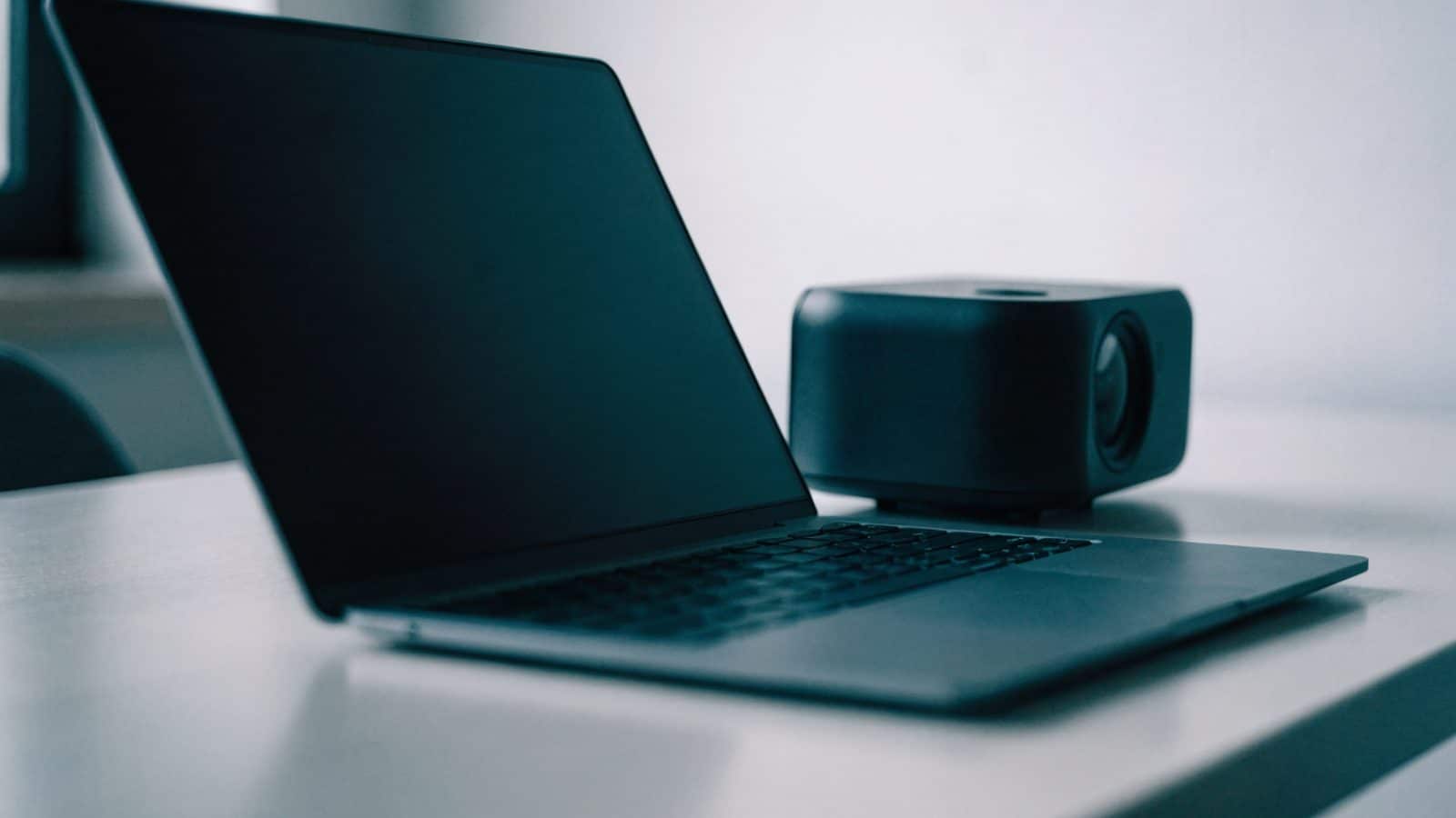 A matte grey laptop beside a small projector on a table