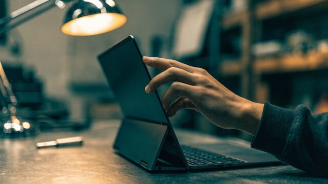 A hand touching the screen of a convertible graphite black laptop folded in tent mode on a workbench